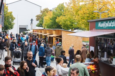 Blick über den belebten Marktplatz mit Holzbuden und der katholischen Kirch im Hintergrund